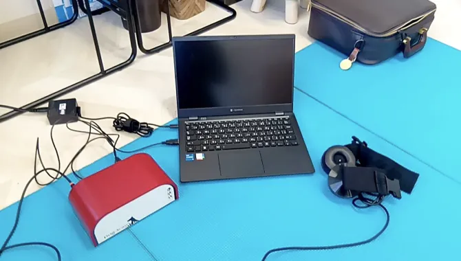 青いマットの上にノートパソコン、赤い機器、ヘッドセットが置かれている。