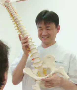 院長が脊椎と骨盤の模型を持ちながら患者に説明している。