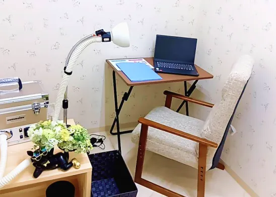 壁に犬の模様が描かれた部屋の一角に、木製の椅子とノートパソコンが置かれたデスクがあり、横にフレキシブルアームのランプが設置されている。